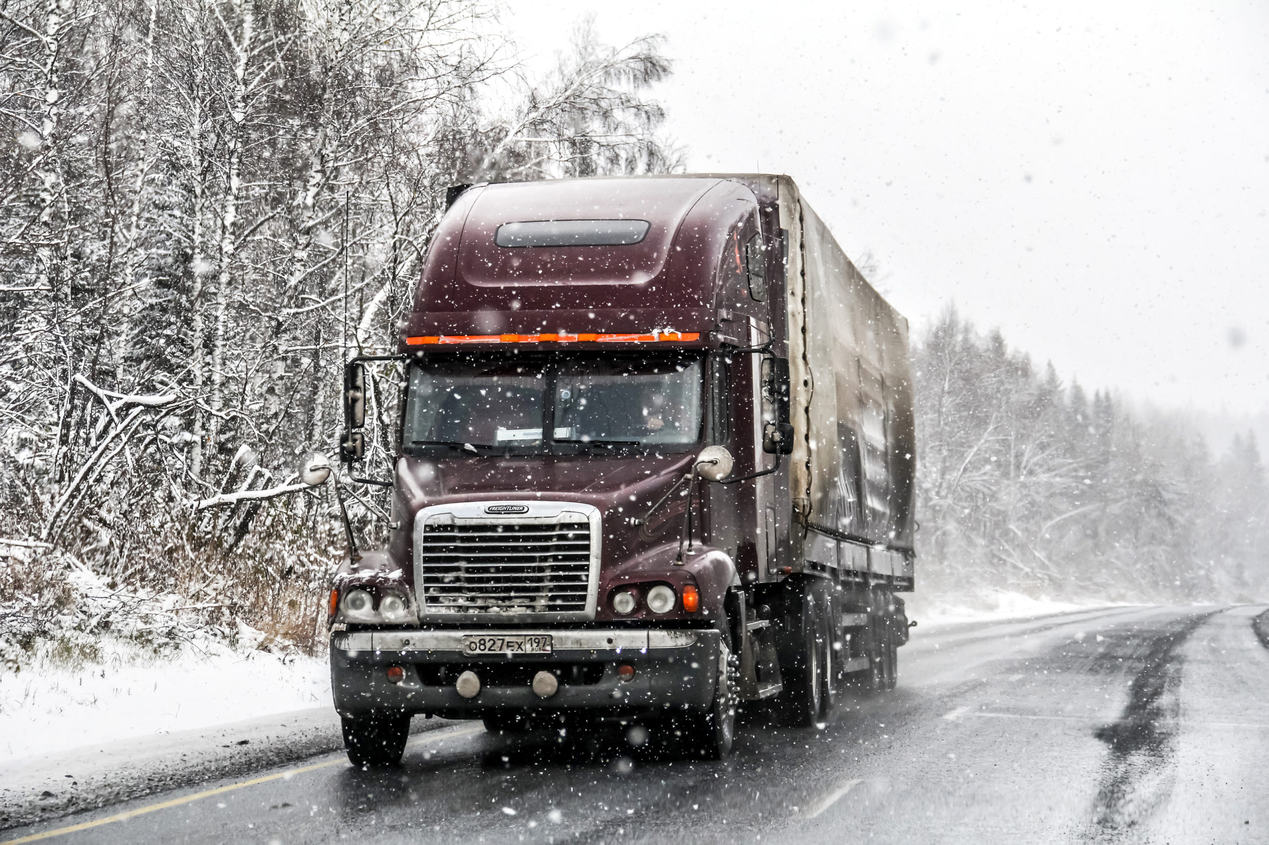 A semi-truck drives through snowy weather