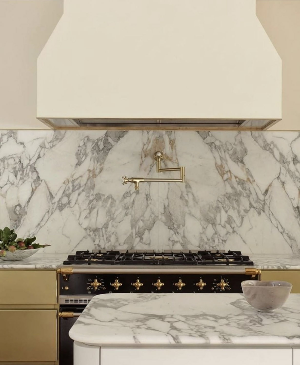 Image shows luxury kitchen interiors with exposed rangehood and marble countertops. The image clicks through to a kitchen interiors trend report 2022. The interiors on the image are designed by Interiors by Arent & Pyke. 