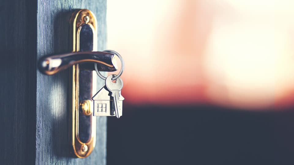 closeup of house keychain and house key on key ring, hanging on front door handle