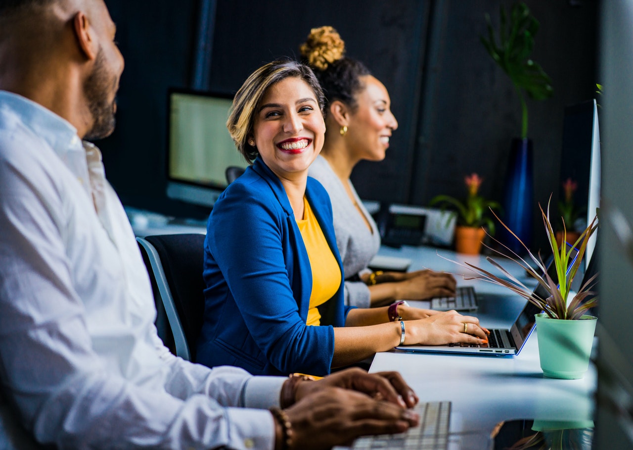 Coworkers smiling at a desk working on their laptops