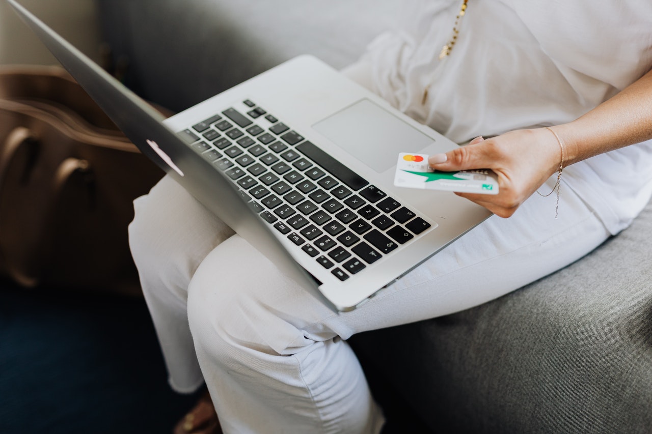 A person sitting with a laptop on their lap, while holding a credit card