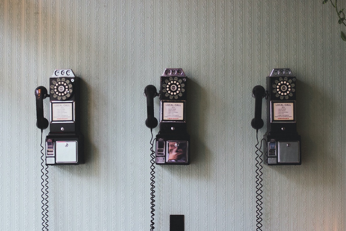 An image of 3 rotary phones on a white wall
