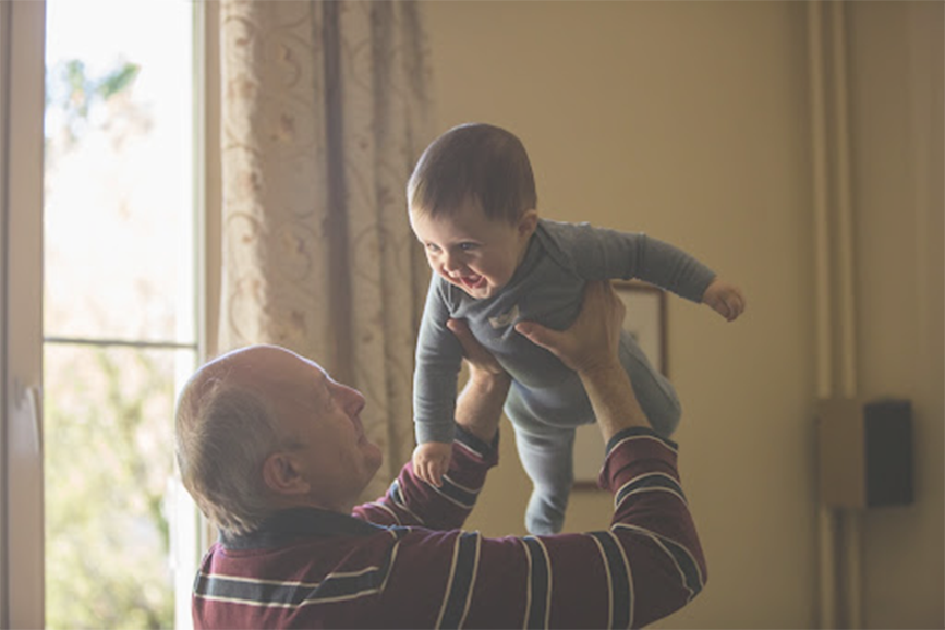 Grandfather in his living room lifting a laughing baby in a onesie