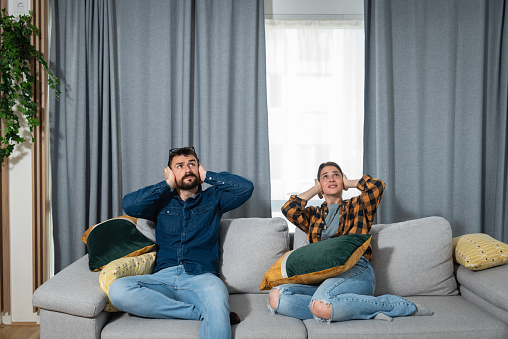 Couple sitting on the couch covering their ears