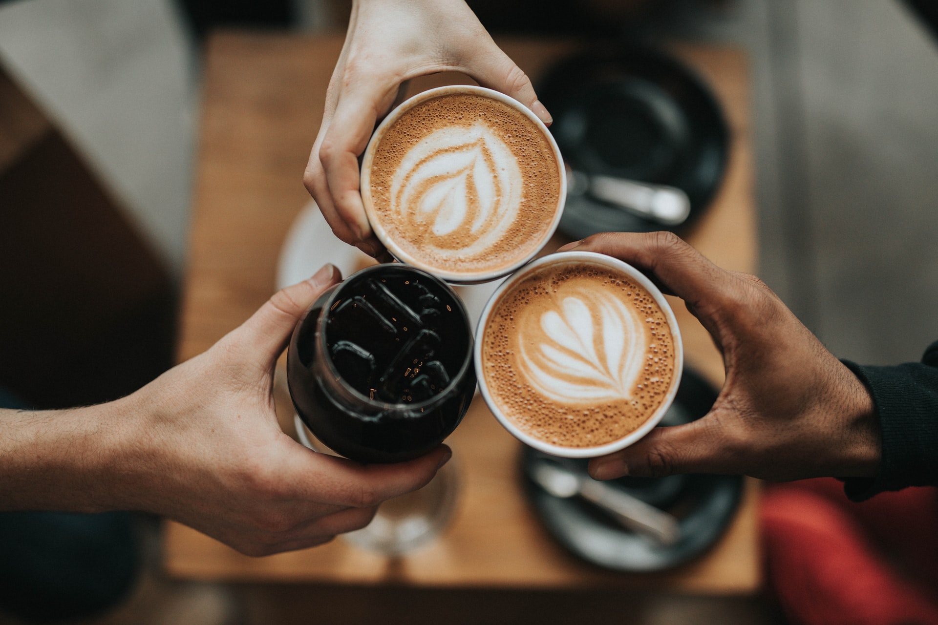Top-view photo of three hands joining three cups of coffee in the middle of the shot