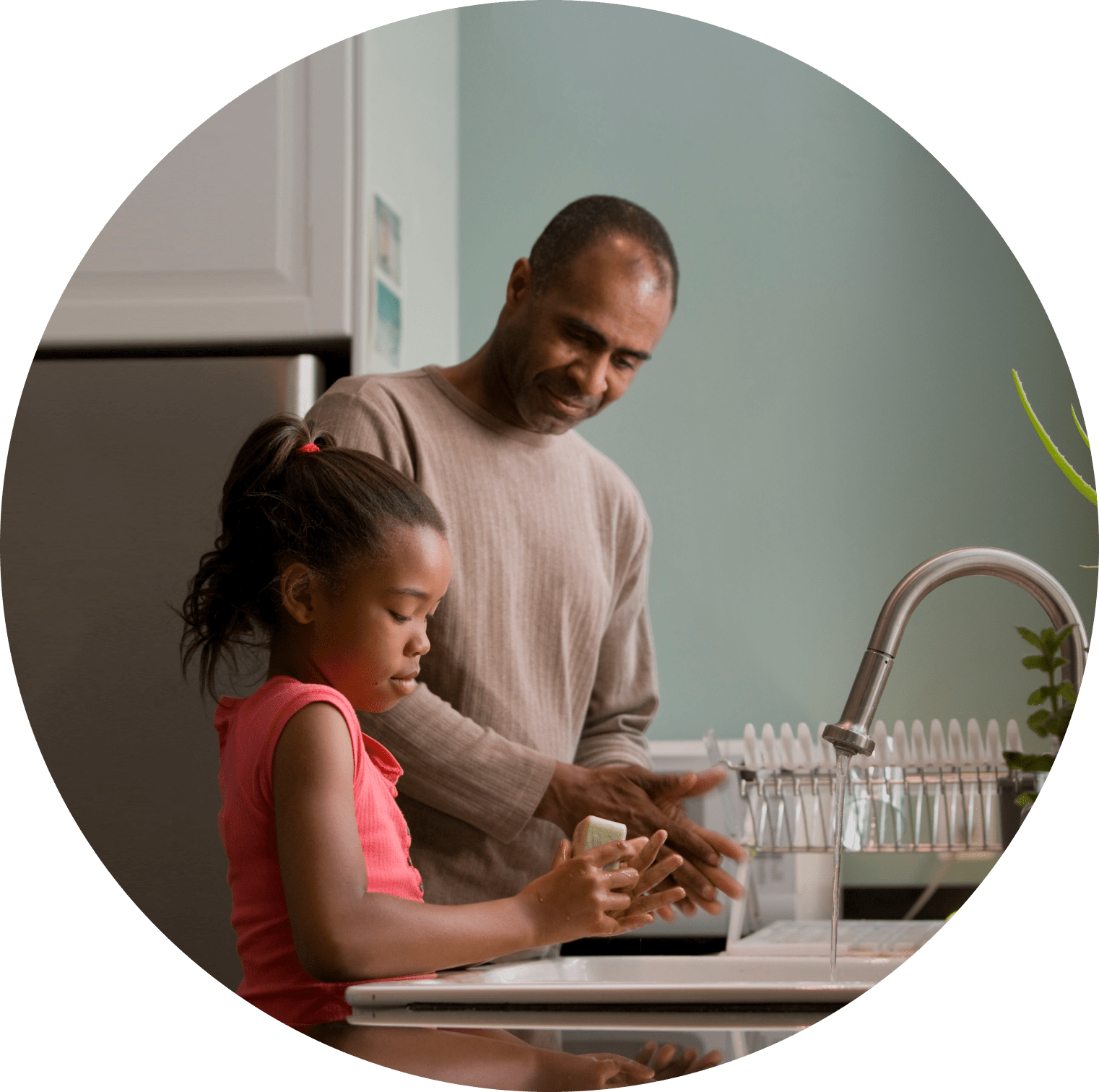 A dad and his young daughter stand at the kitchen sink washing their hands.