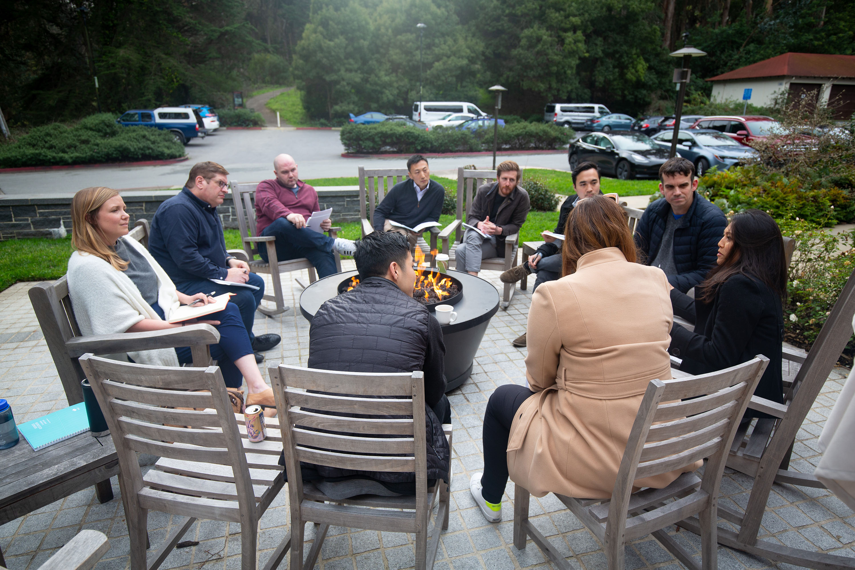 A group of Praxis fellows engaged in discussion seated in a circle around a fire pit.