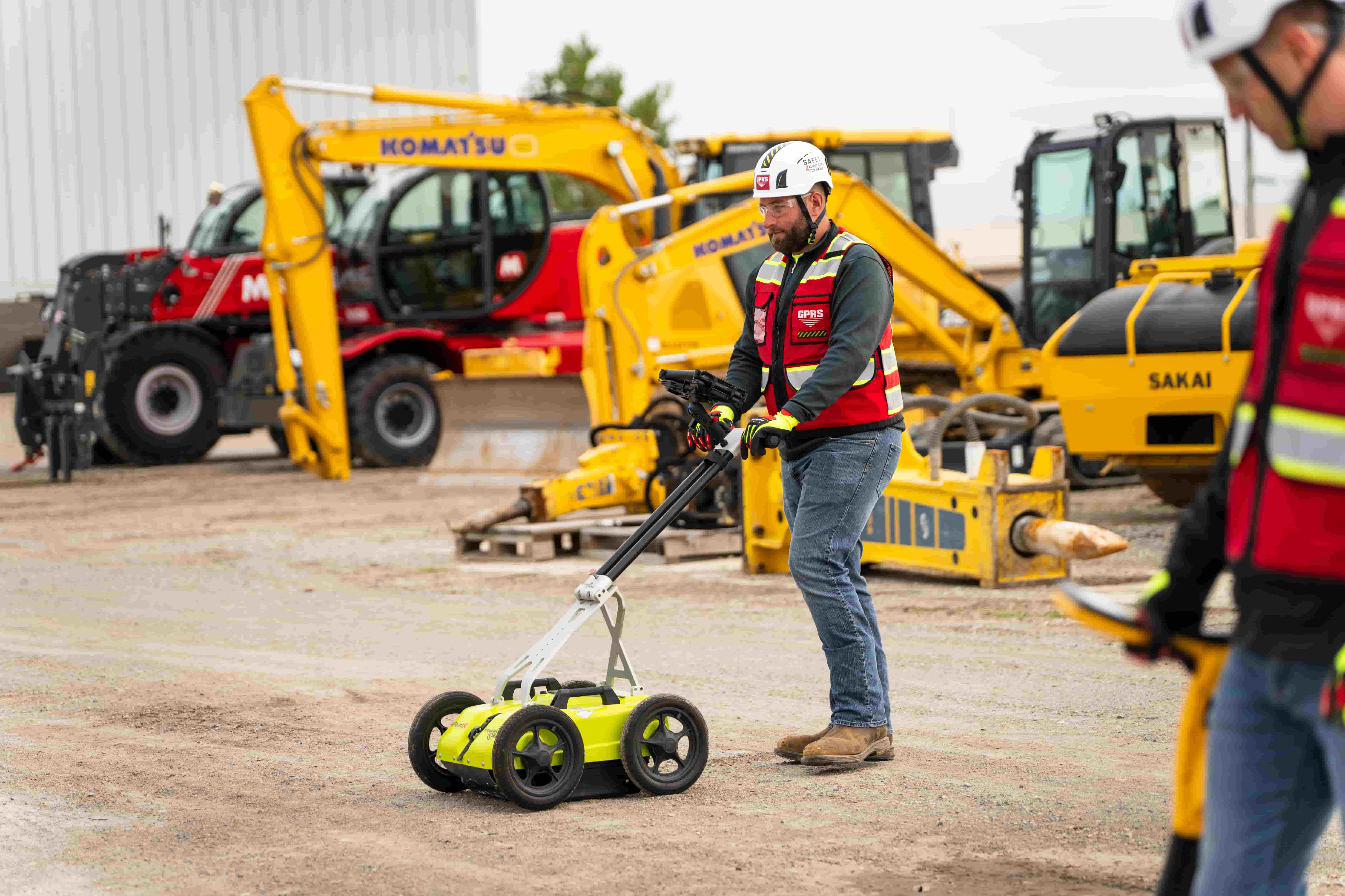 A worker in personal protective equipment pushes a ground penetrating radar scanner through a construction site.