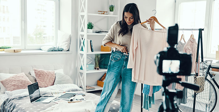 A woman is trying on different items of clothing including jeans and a sweater from fashion brands.