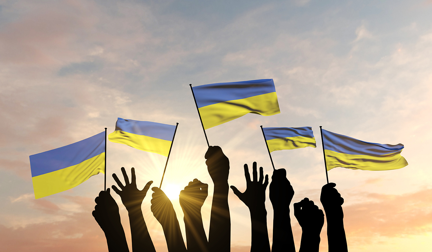 4 Ukranian flags raised by silhouetted hands.