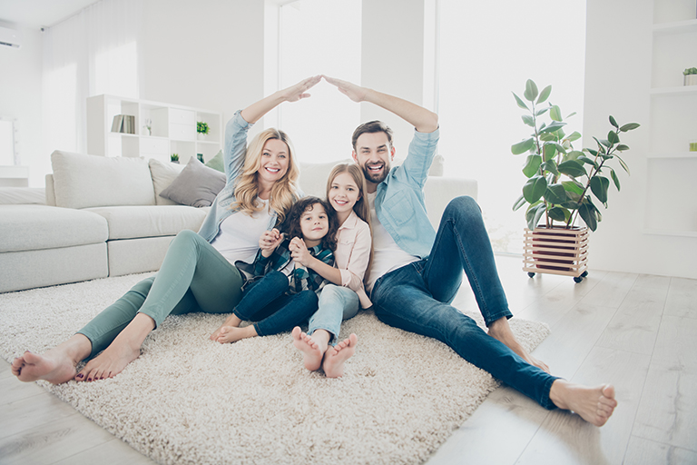 Family sits together on floor forming roof with hands