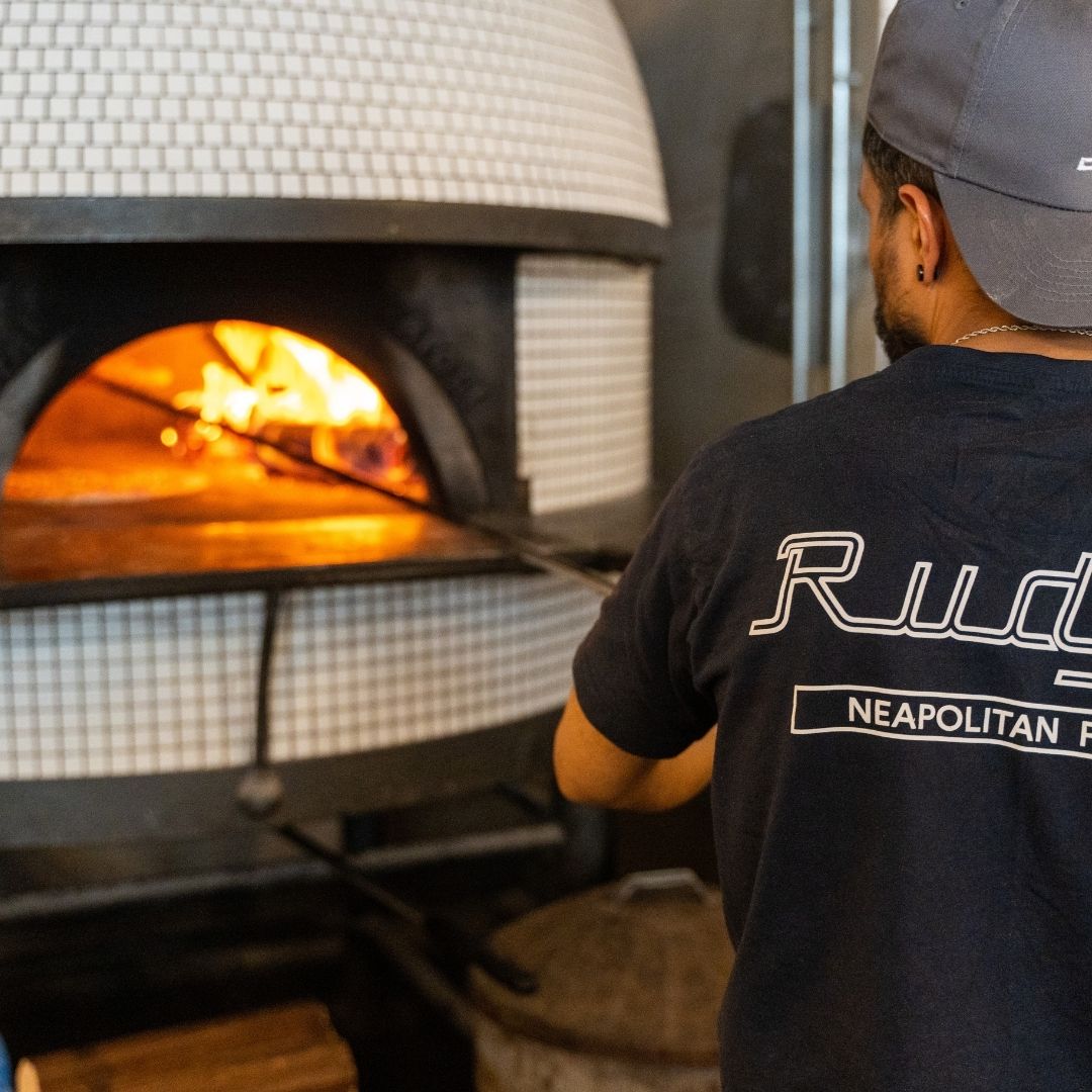 picture of rudy's pizzaiolo putting a pizza in the oven