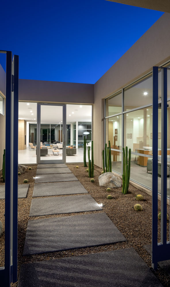 A modern minimalist residential home entrance foyer with open air skylight, cactus garden and professionally styled furniture and decor shot at dusk with available light.