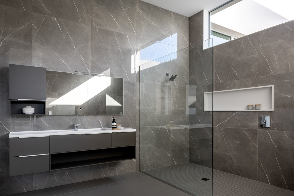 A modern minimalist bathroom with neutral colors and marble walls featuring a shower and window lit by natural light during the day.