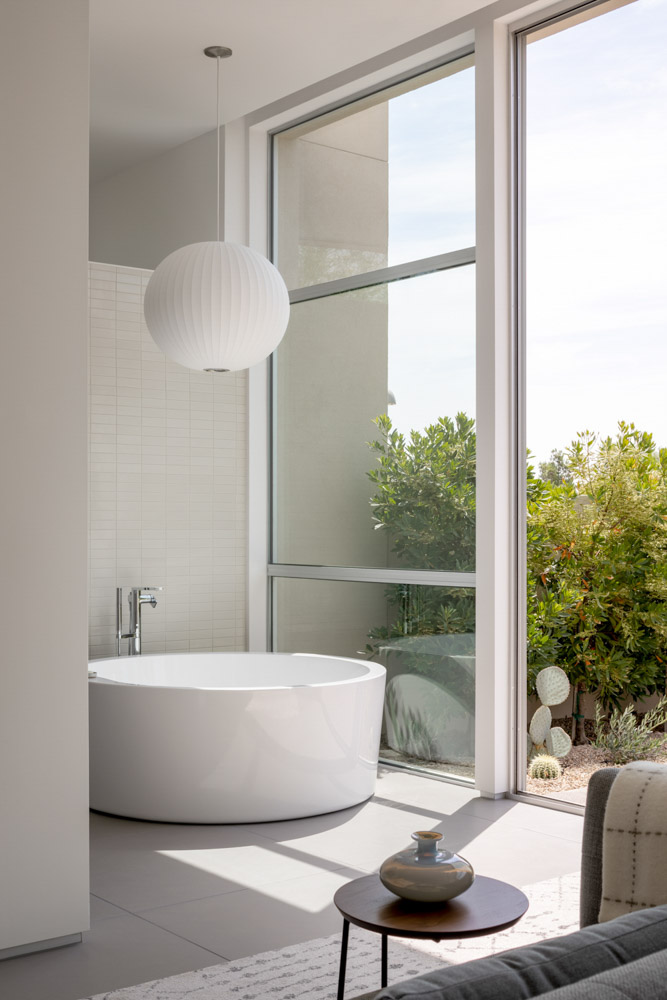 A modern minimalist residential home featuring a bedroom with a bathtub with sunlight streaking in all lit by natural light.