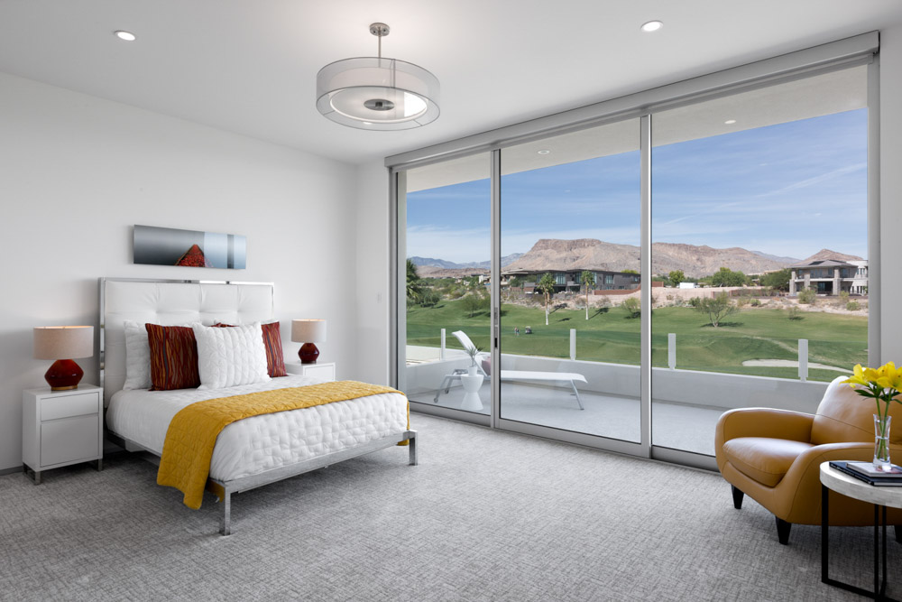 A modern minimalist residential bedroom with contemporary furniture and a patio overlooking a golf course fairway and mountains in the background.