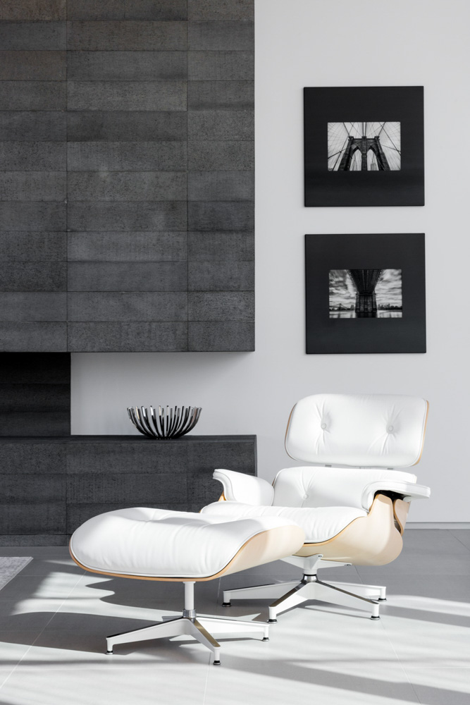 A modern minimalist residential livingroom featuring a fireplace and an original herman miller eames lounge chair and ottoman shot during the day with natural light.