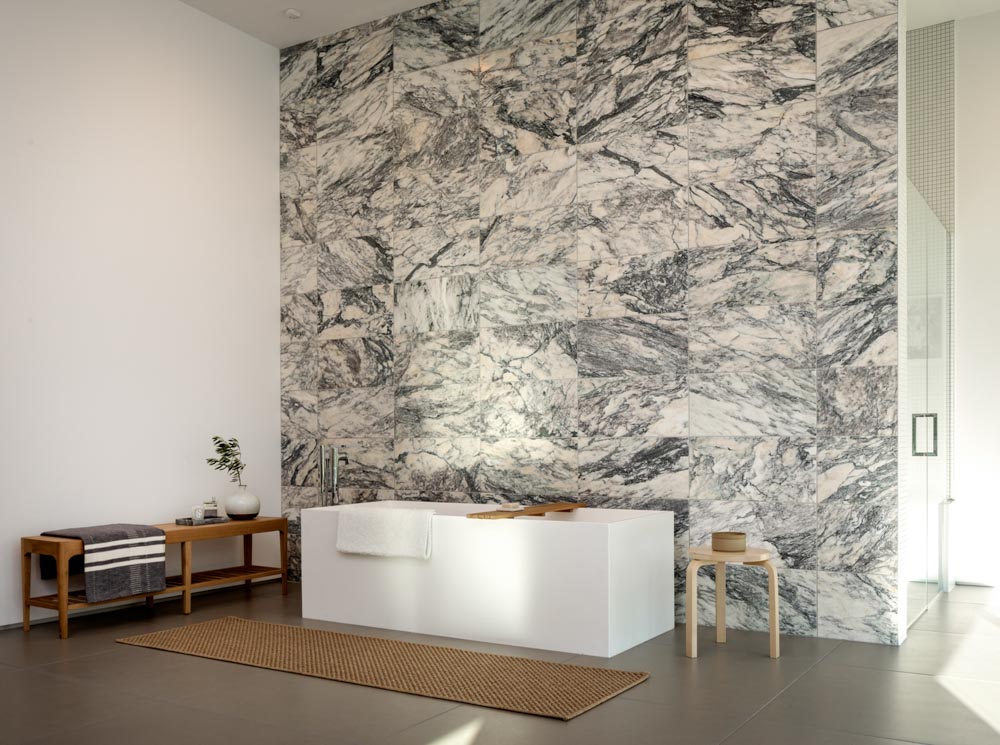 A modern minimalist residential master bathroom with neutral colors, marble, natural wood and a japanese style soaking tub shot during the day with natural light.