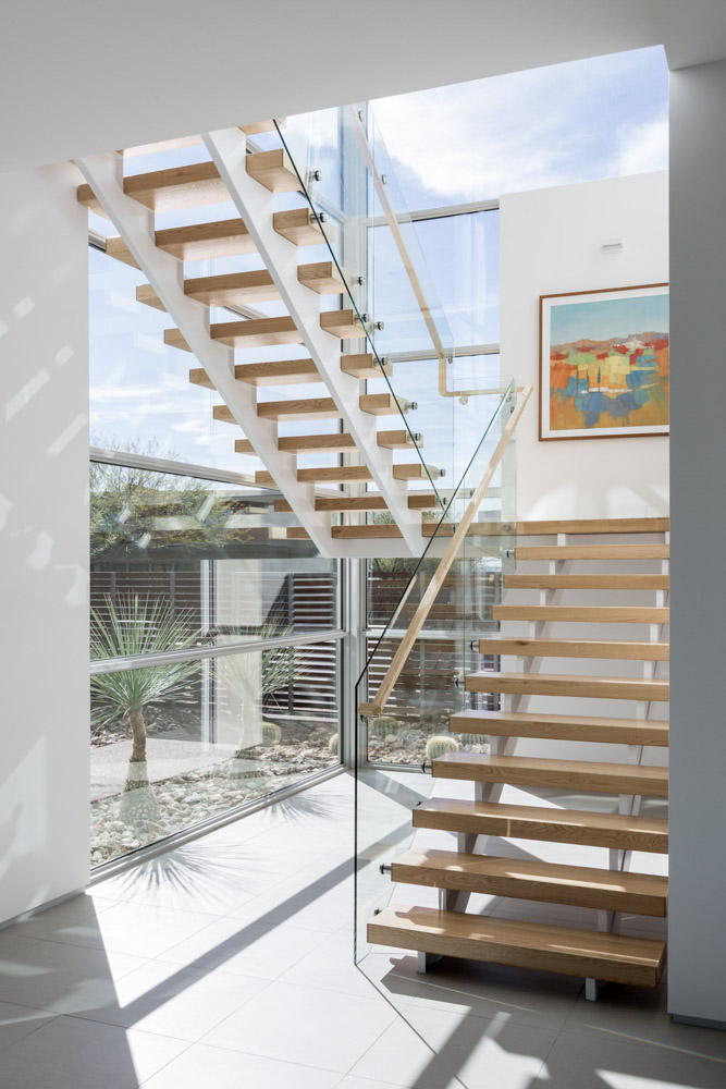 A modern minimalist residential home with a natural wood staircase surrounded by panoramic windows bright with natural light during the day.