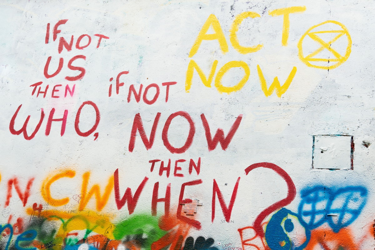 A white wall, with graffiti saying 'If not us then who, if not now then when?' and 'Act now'