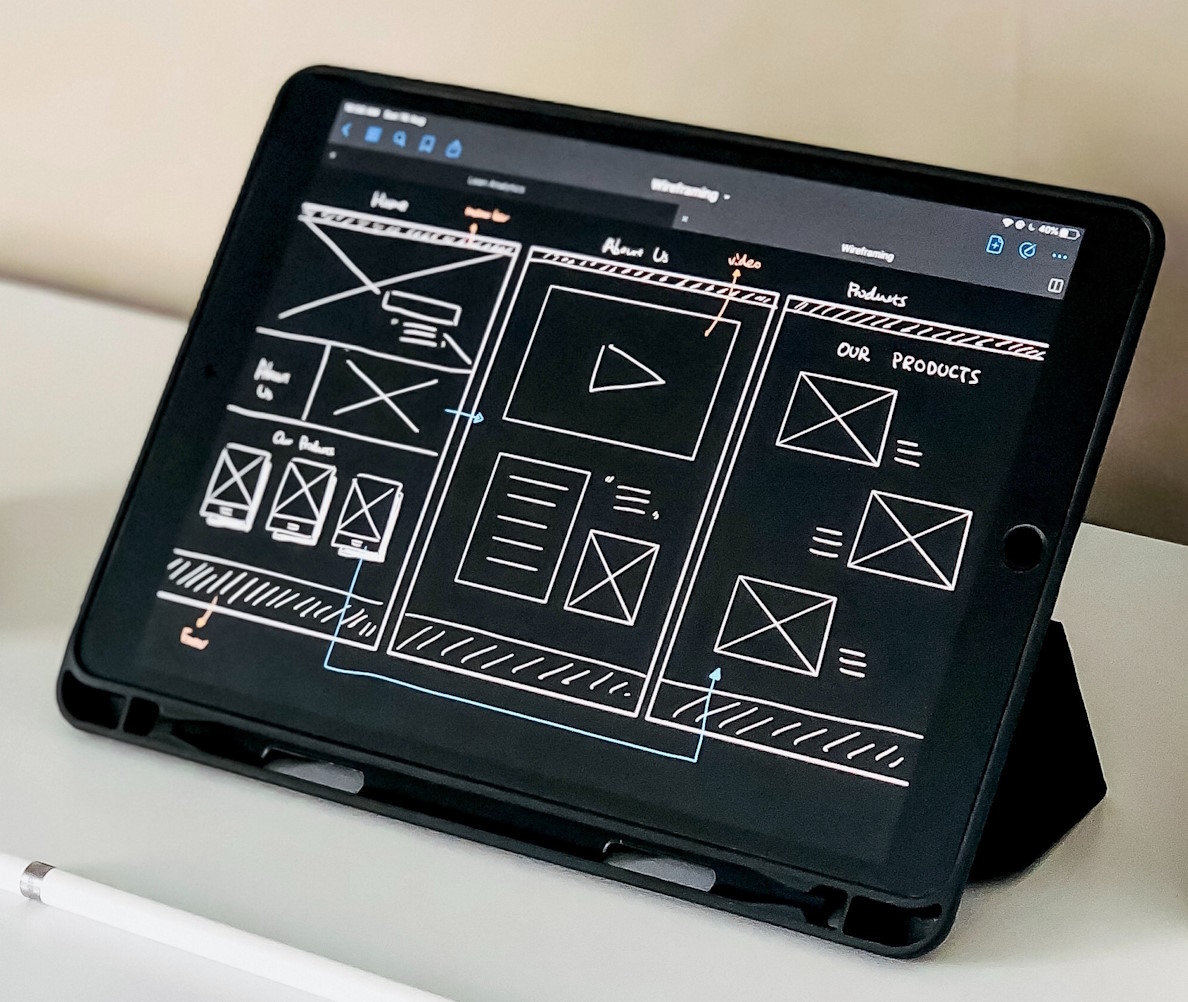 A website wireframe showing high contrast black background with white elements like forms, titles and boxes for images. On a tablet standing on a table. 