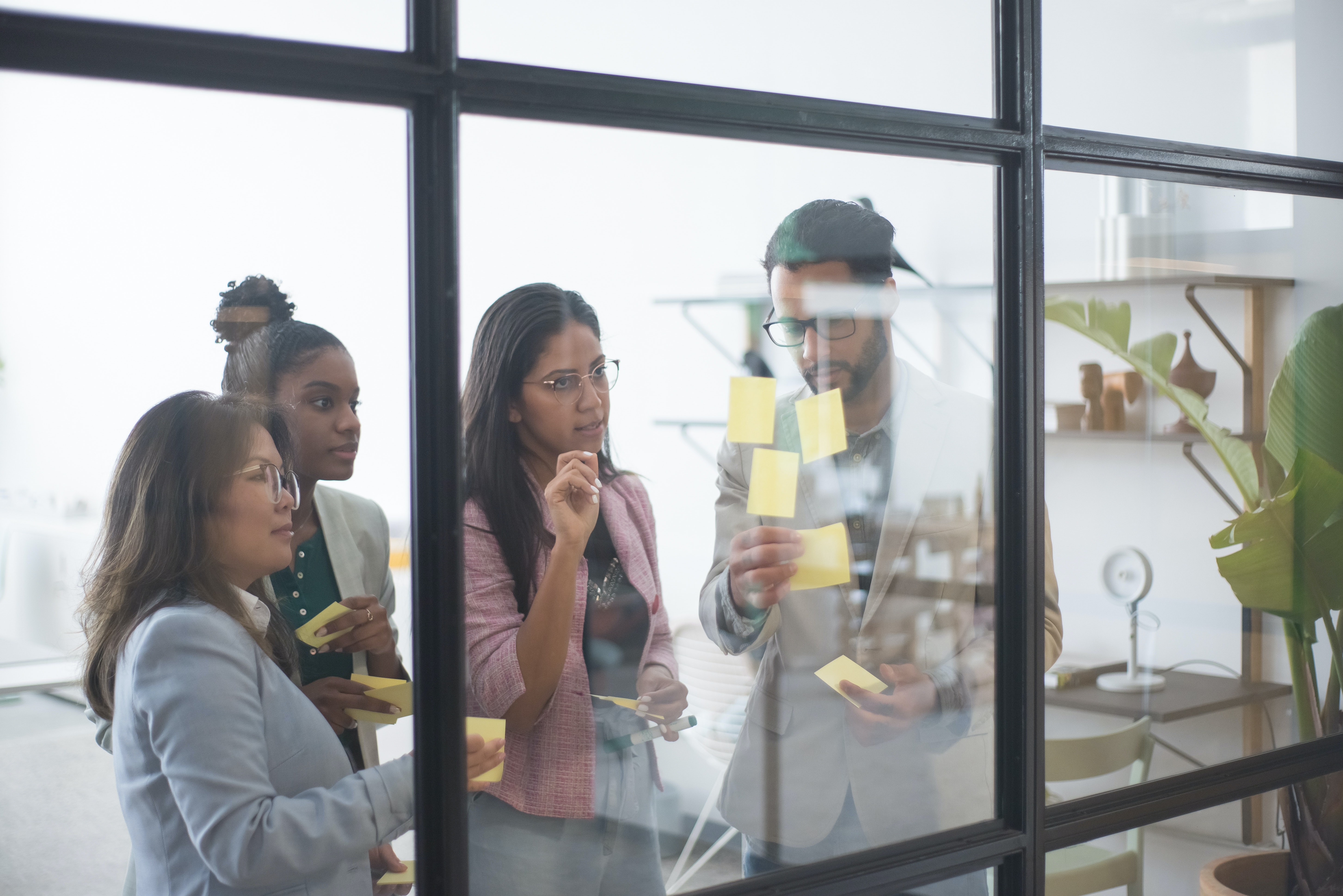 Team members working out problems in a visual way with post-its and a clear glass window to draw on.