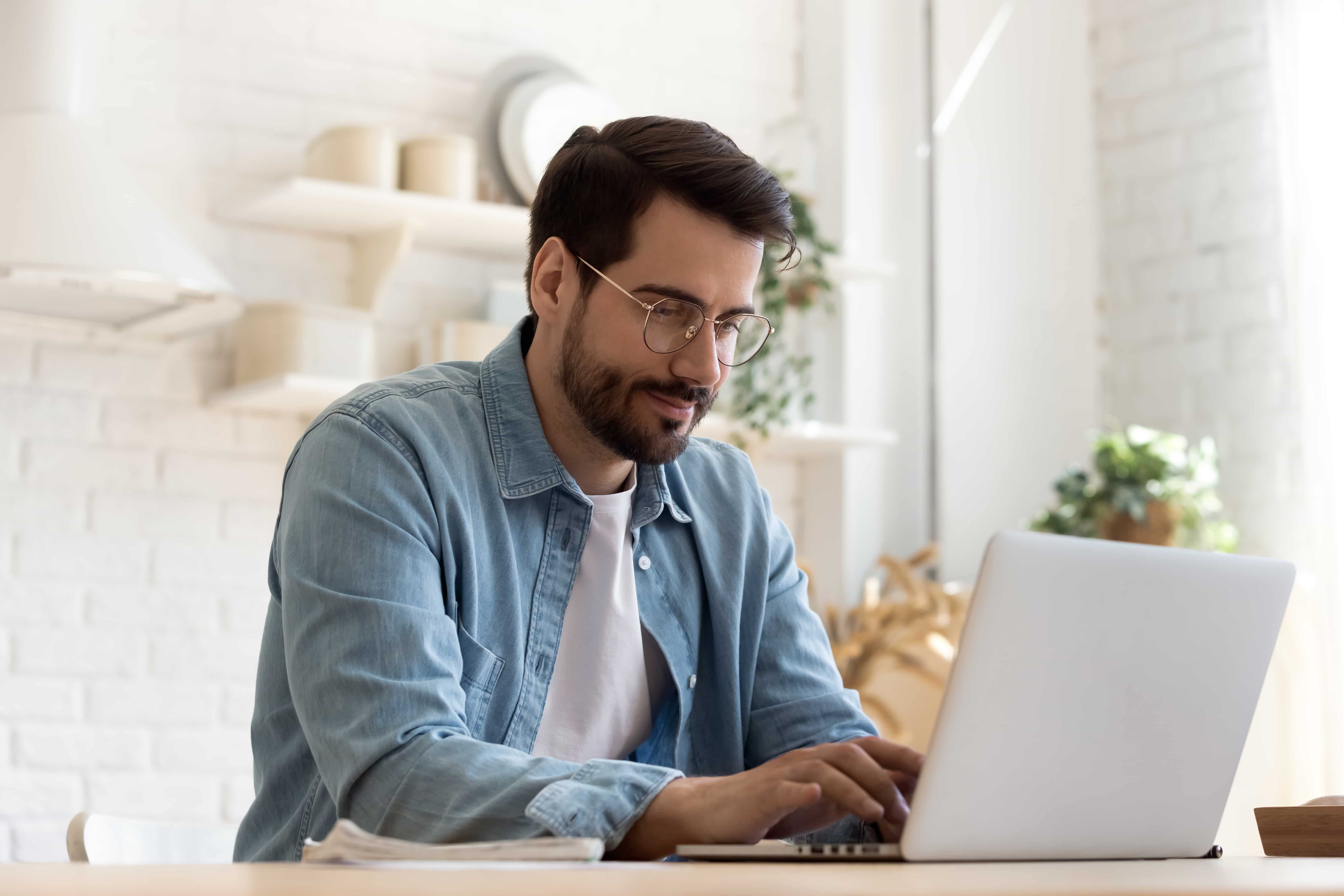 A young professional looking man writes a modern CV on his laptop