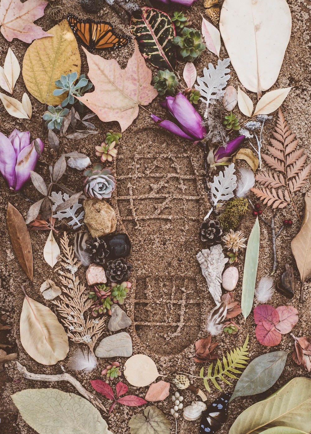 Close up of a footprint in sand, surrounded by autumn leaves