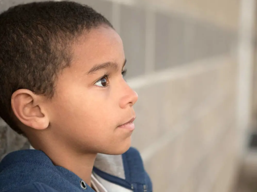 A young boy leaning against a brick wall looking worried