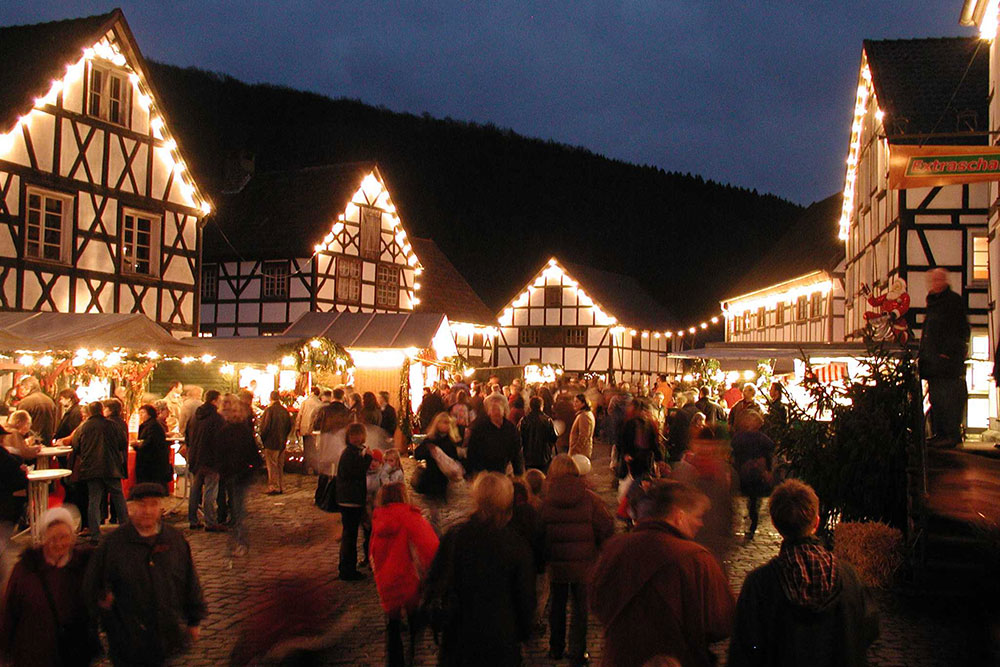 Besucher*innen vor illuminierten Fachwerkhäusern und geschmückten Hütten, Freilichtmuseum Hagen, Ruhrgebiet 