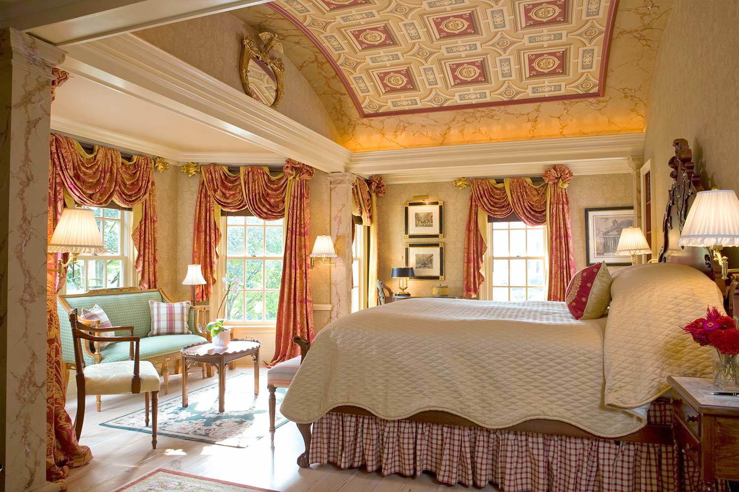A very large master bedroom with a king sized bed, sitting area and ornate ceiling.