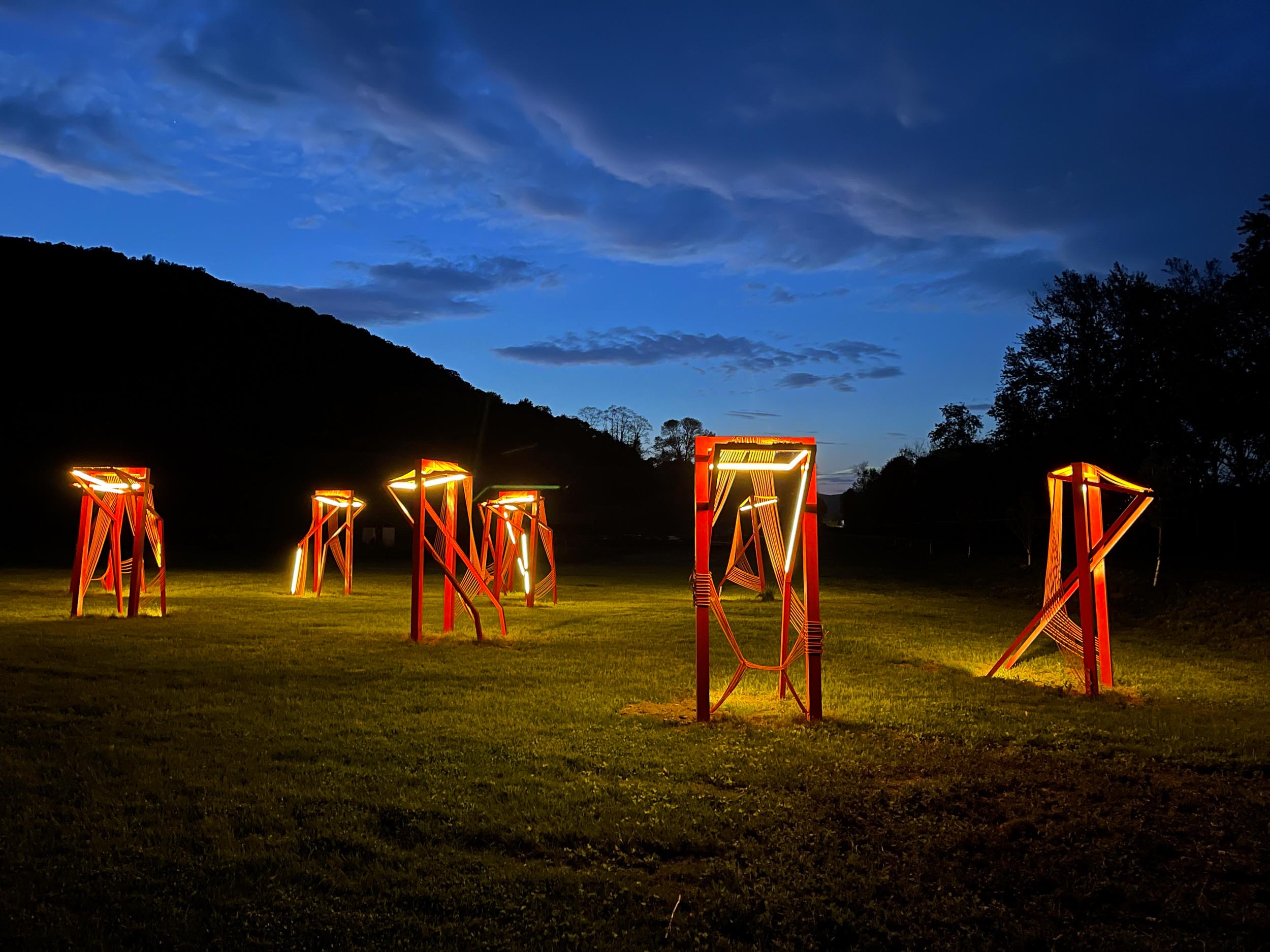 Six glowing red steel-frame sculptures in a field at night.