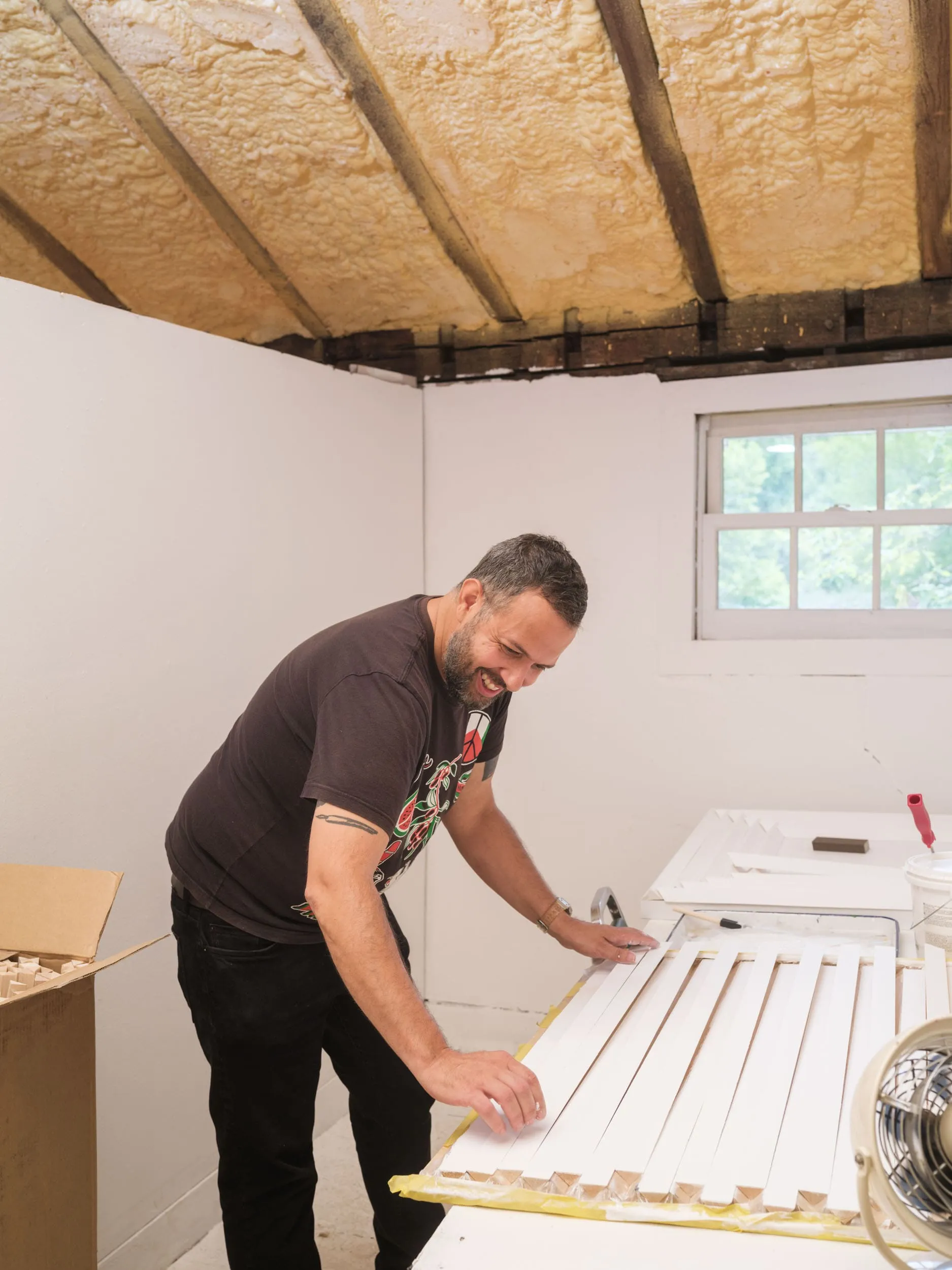 A man smiles while standing hunched over an in-progress artwork in his studio.