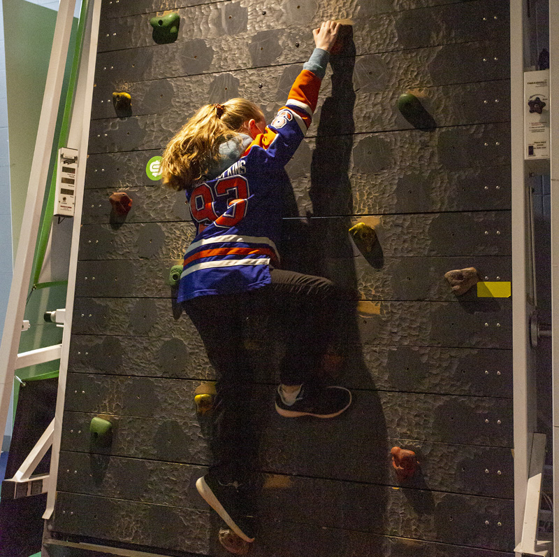 Youth climbing the tread wall at the Alberta Sports Hall of Fame while wearing a hockey jersy