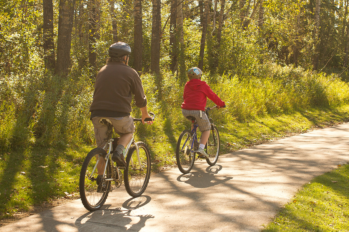 A pair of bike riders using a paved trail through the trees of Waskasoo Park