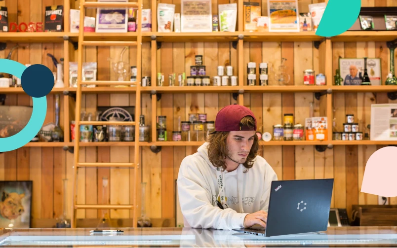 A dispensary manager is standing behind a counter with his laptop to create his 420 staffing plan.