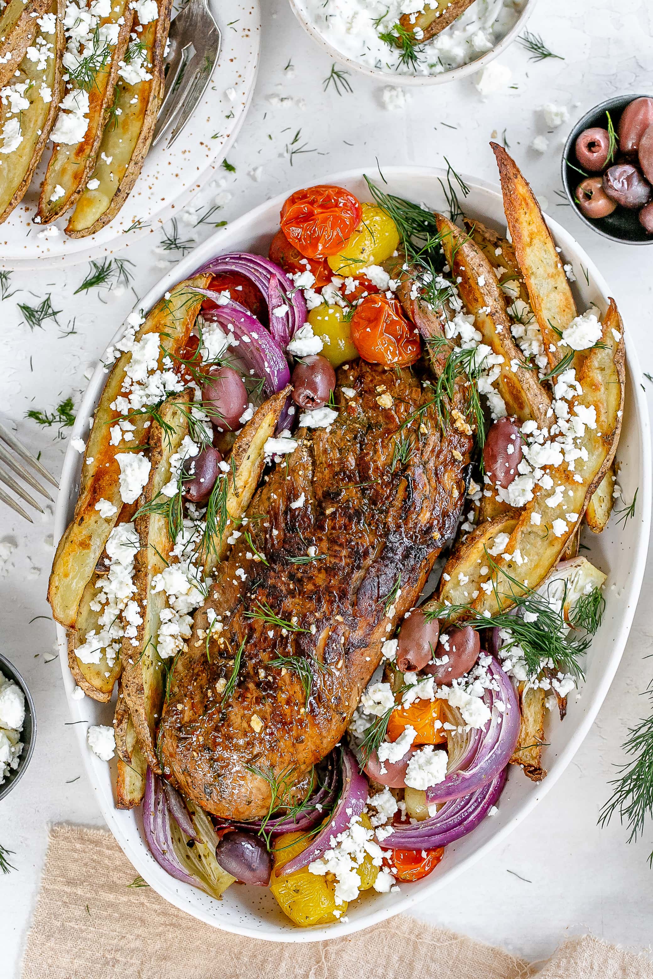 Greek pork tenderloin on serving platter with fries and veggies. 