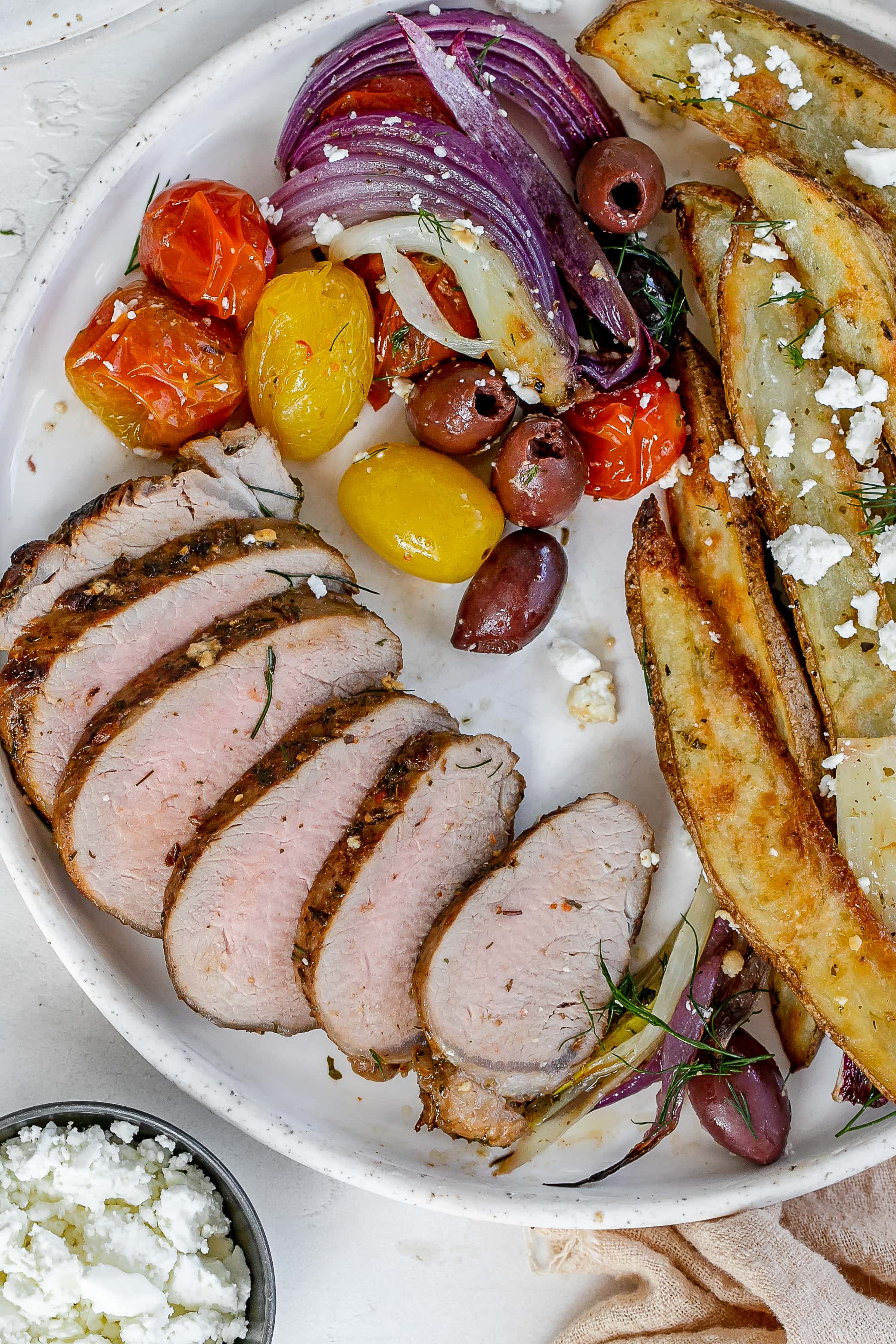 Greek pork tenderloin on a plate with fries and veggies. 