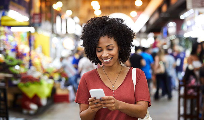 Woman smiles at her phone while stopped in a busy indoor market
