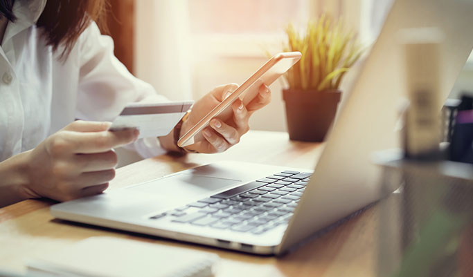 Woman at laptop phone in one hand and credit card in the other
