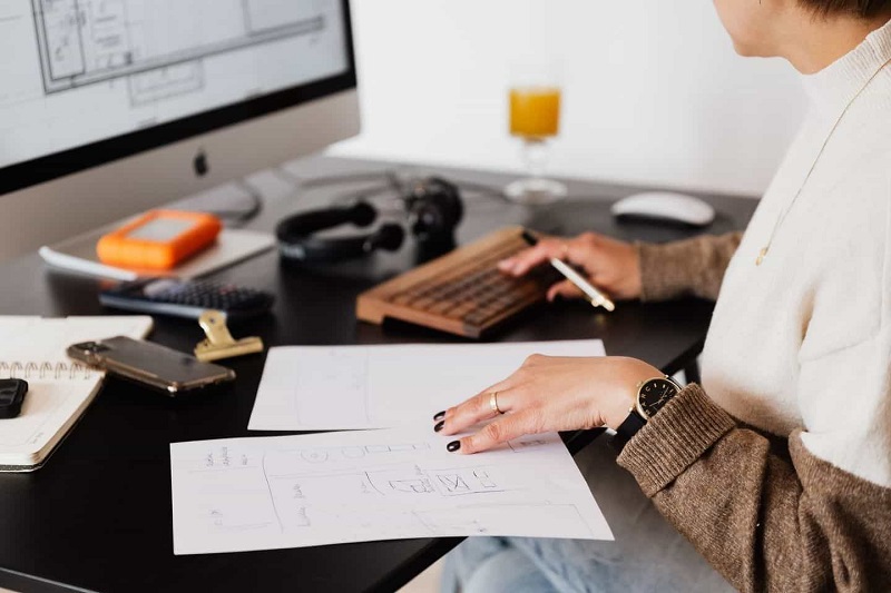 A women is writing in paper looking at computer.