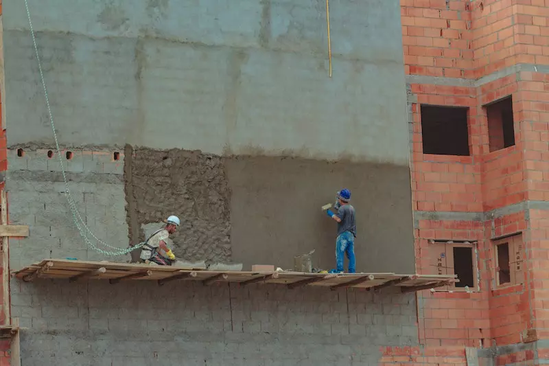 2 man applying cement on building 