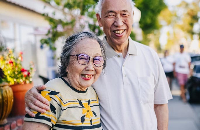 A couple smiling for a photograph on a tree-lined street