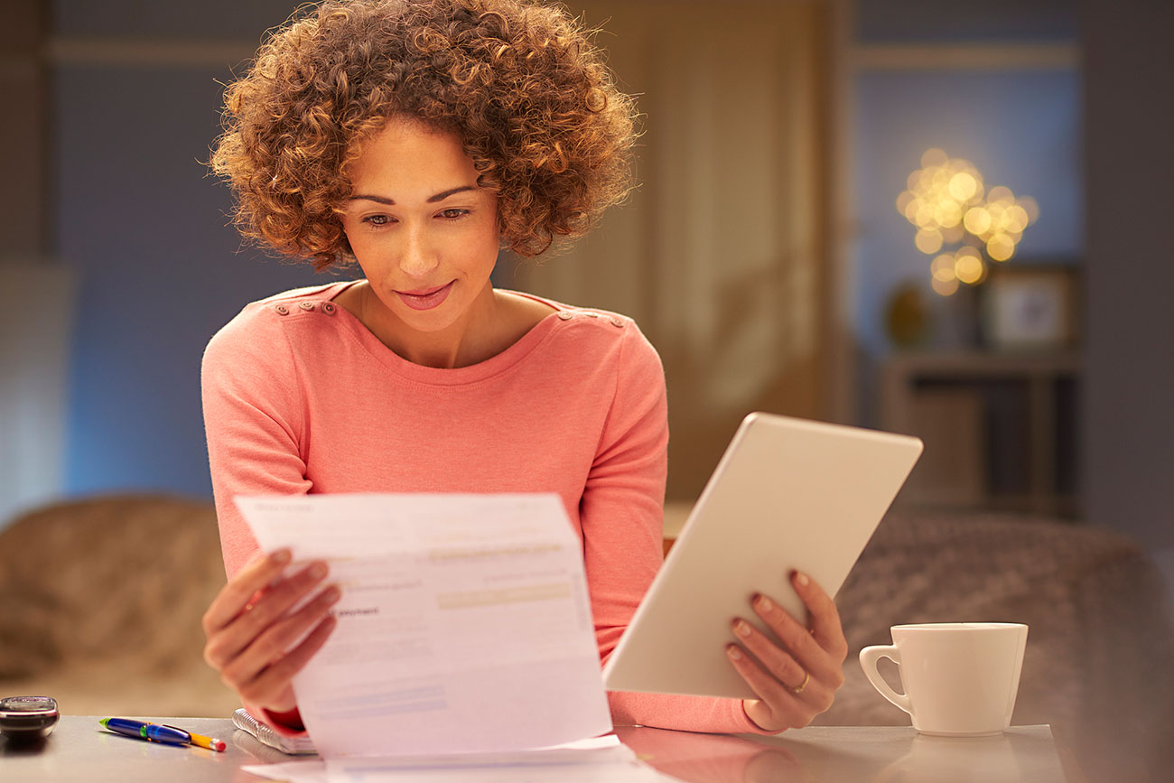 a young woman sits at home at night calculating self-employed taxes|Woman looking at forms: Calculating self employed taxes