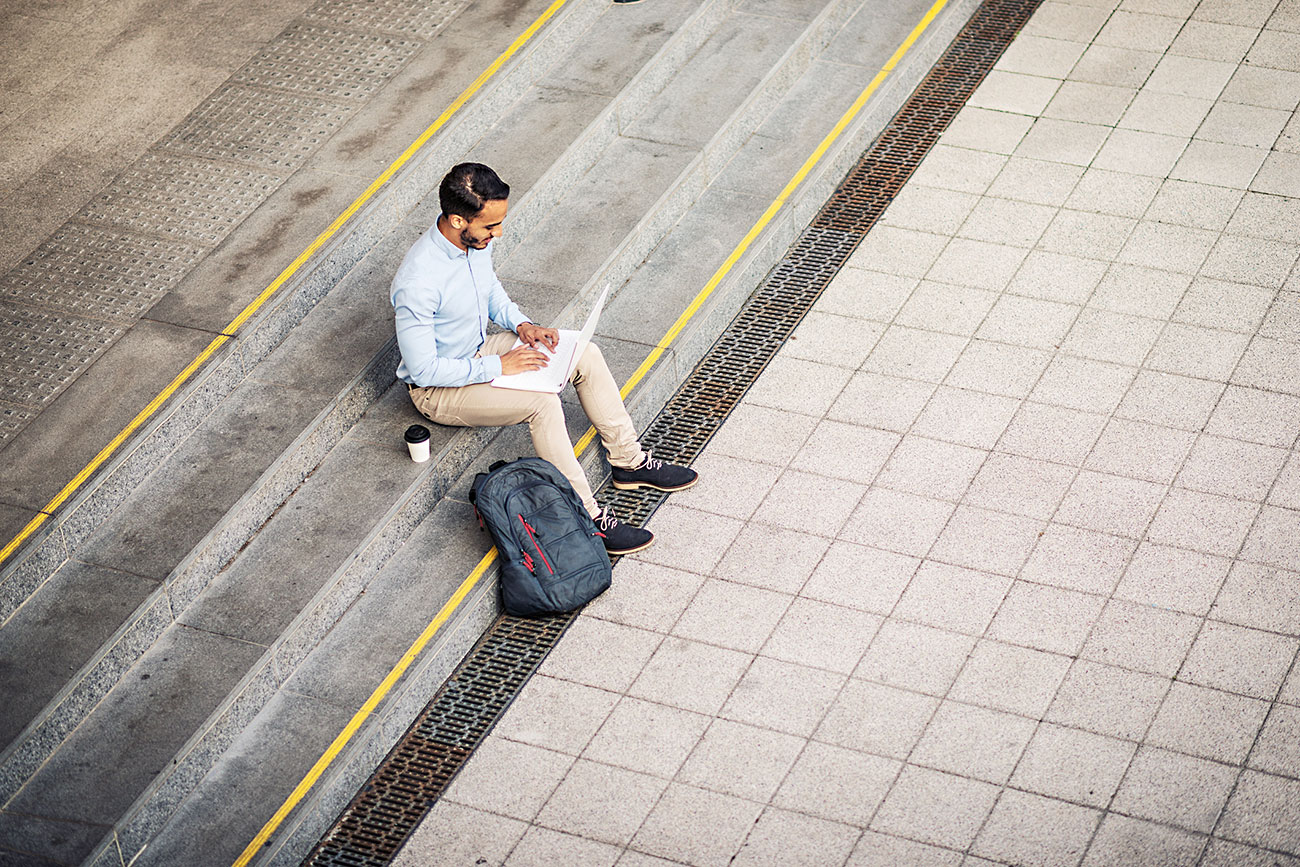 Self-employed Latino businessman seated on steps of central train station using public wi fi|A closed sign in a shop