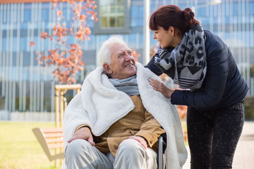 A woman wrapping a blanket around a man in a wheelchair