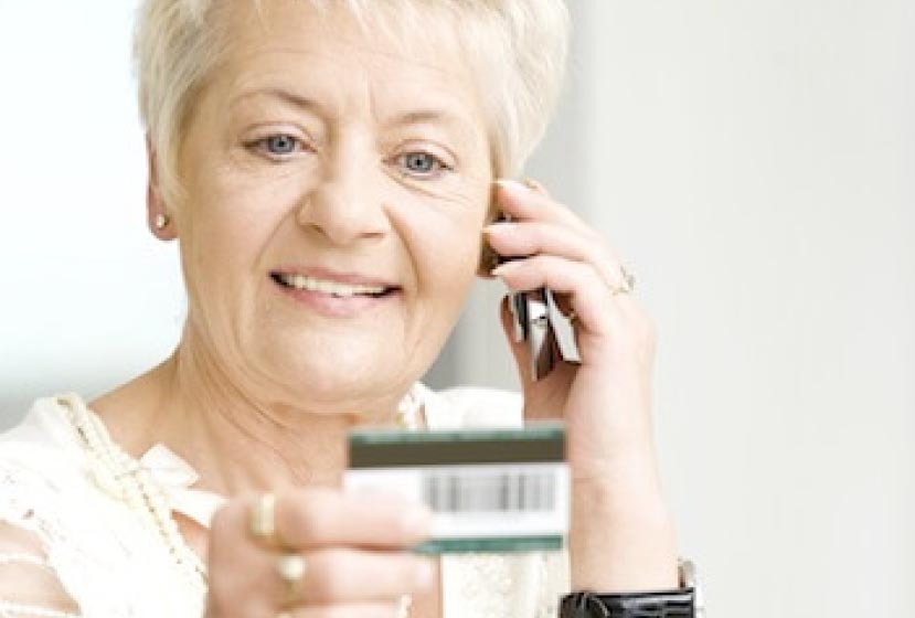 A woman looks at her credit card while on a phone call