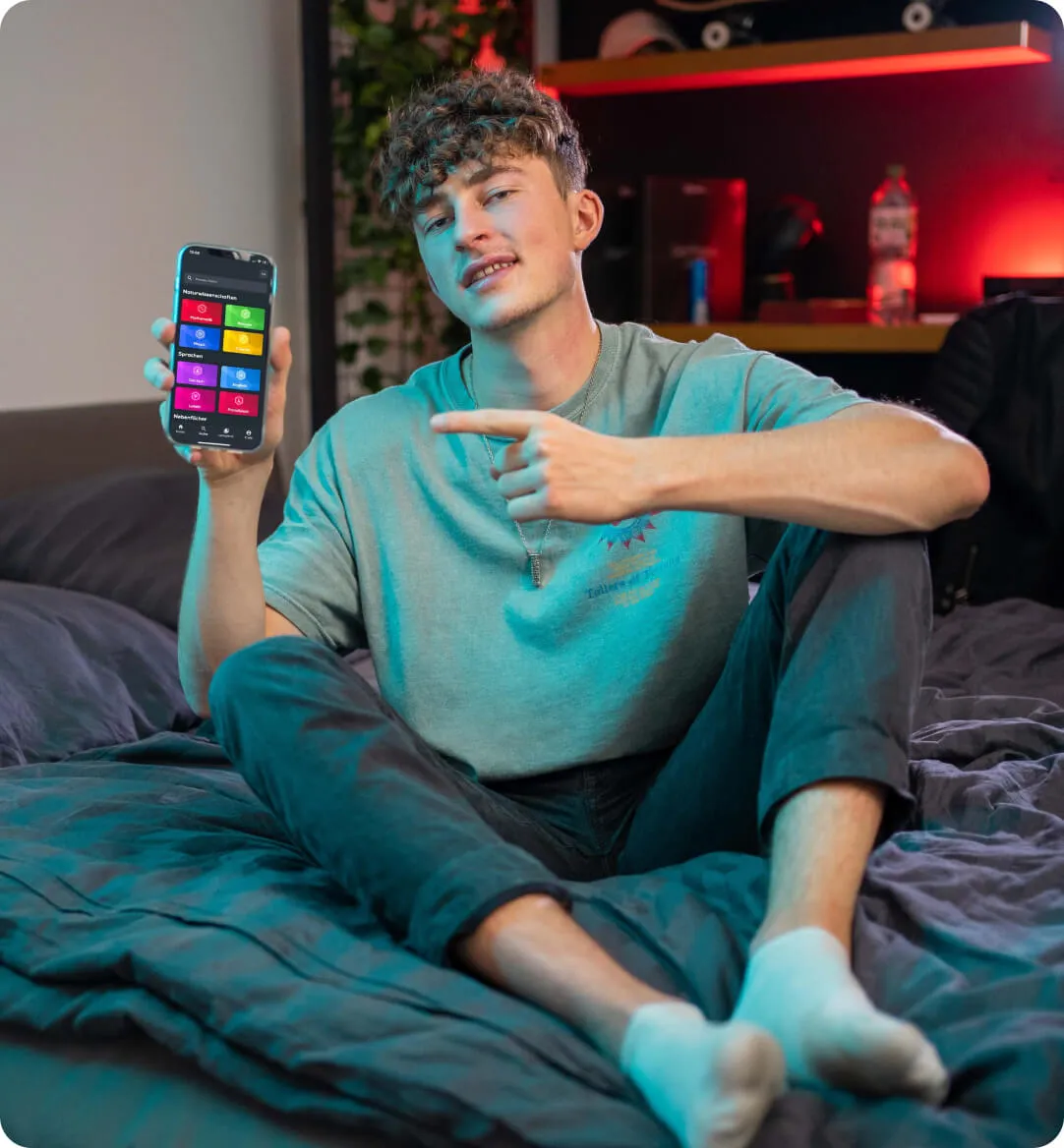 Man with curly hair is siting on the bed and pointing on the cell phone where is open Simple Club App - Simple Club