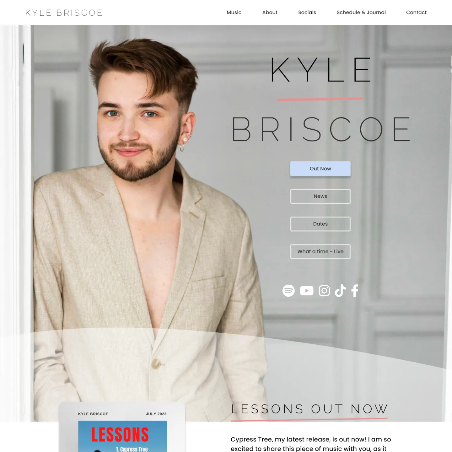 A photo of Kyle Briscoe, a white man with brown hair and blue eyes looking at the photographer, competent and excited to show the world his music. He is wearing a brown blazer over a bare chest.