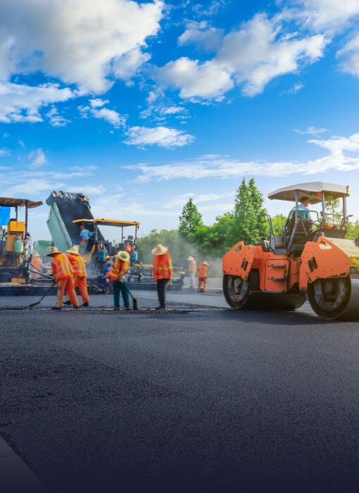Workers paving a road under a bright blue sky
